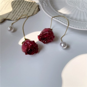 Macro view of long gold drop earrings with red rose charm and white pearl detail