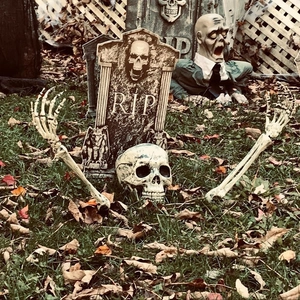Detailed view of Halloween tombstone, skeleton skull and hands on dry autumn leaves
