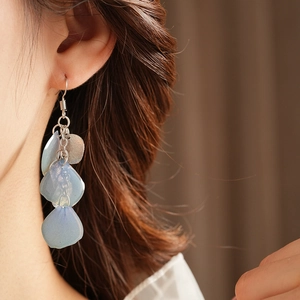 Dettaglio ravvicinato di orecchini a nappa con conchiglia blu su modella per look da spiaggia