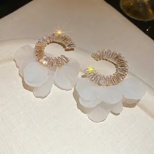 Golden C-shaped hoop earrings with zircon stones and white flower petals on fabric
