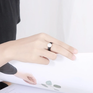 Detail of a minimalist black band ring featuring a large white pearl worn on a hand