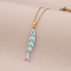 Macro shot of gold necklace with white and turquoise enamel fish pendant on beige fabric