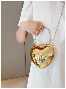 Close-up of golden heart-shaped acrylic clutch bag with metallic handle and chain strap