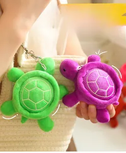 Luminous plush turtle keychains in green and purple colors on a beige woven bag