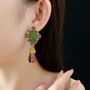 Detail of vintage gold earrings with green relief stone and red crystal teardrop