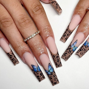 Detail of long coffin press-on nails featuring nude base with leopard tips and blue butterflies