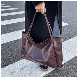 Detailed street shot of a large dark brown faux leather tote bag with glossy oily finish