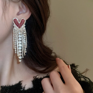 Close-up of model wearing luxury silver heart earrings with red rhinestones and long tassels