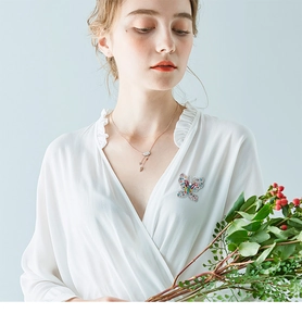 Detail of colorful butterfly brooch featuring crystal inlay on white V-neck blouse