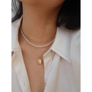 Layered gold necklace set with pearl strand and rose embossed oval pendant on a white shirt