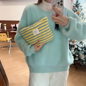 Detail of soft plush yellow and blue striped makeup bag with zipper held by model