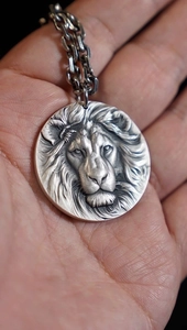 Macro shot of a silver lion head medallion pendant held in hand with fine carving details