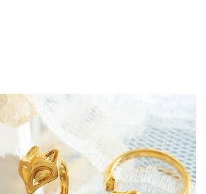 Detailed macro view of an adjustable gold-plated fox head ring on a soft lace background