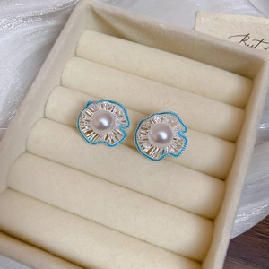 Close-up of pearl flower earrings with blue enamel petals on a jewelry box display