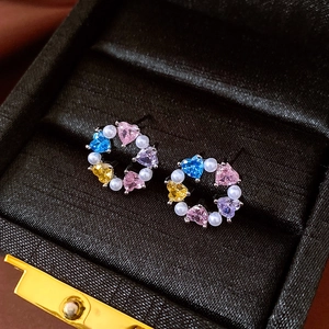 Detail of heart-shaped colorful zircons and white pearls in a circular earring design