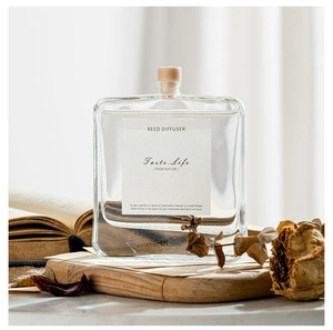 Square glass reed diffuser bottle with wooden stopper in a cozy interior setting