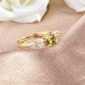 Elegant gold ring with olive green zircon and white crystals on champagne silk background