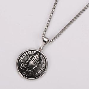 Macro detail of silver stainless steel necklace with praying hands and Latin engraving