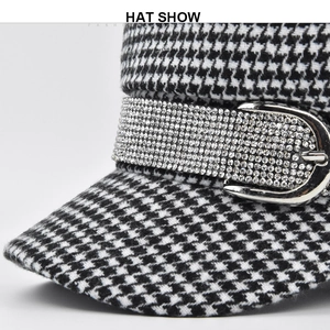 Detail of black and white houndstooth hat featuring a rhinestone strap and metal buckle