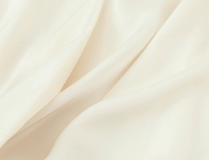 Detailed macro view of cream satin fabric texture and luxurious silk sheen on the blouse