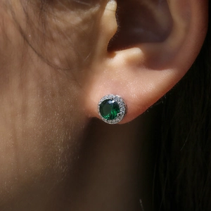 Macro shot of a round halo earring with a deep green gemstone and sparkling white zircons
