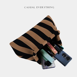 Top view of striped knit clutch bag holding two smartphones and various cosmetics