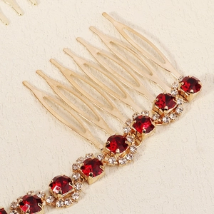 Detailed close-up of golden bridal hair comb with vibrant red crystals and clear rhinestones