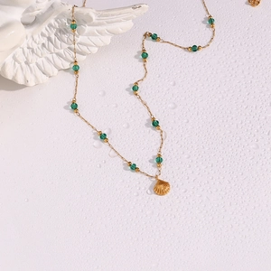Detail of gold chain necklace with green faceted beads and shell pendant on water droplets