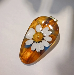 Detail of drop-shaped resin pendant with dried daisy flower and amber dye