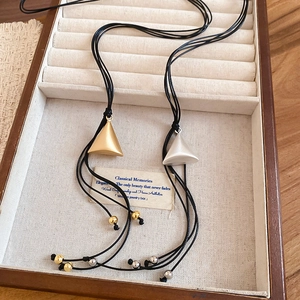 Close-up of matte gold and silver triangle pendants on black multi-strand cord necklaces