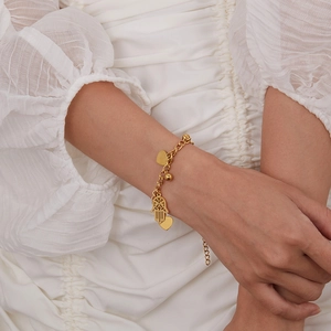 Detail of golden heart and Hamsa Hand charms on a stainless steel chain bracelet
