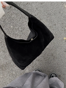 Close-up of black matte suede hobo bag with wide handle and metal buckle on asphalt