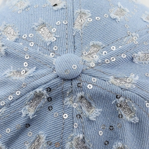 Detailed top view of distressed denim baseball cap with silver sequins and star patches