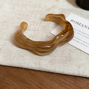 Macro shot of irregular wave resin bangle in amber brown finish on rustic linen cloth