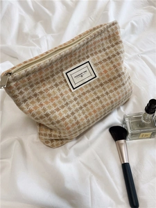 Close-up of checkered tweed makeup bag with a woven tag on white linen fabric