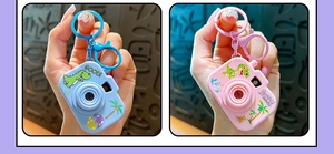 Detailed view of two colorful mini toy camera keychains with cute cartoon dinosaur prints