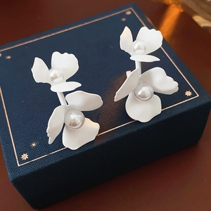 Detailed macro view of C-shaped floral earrings with pearls on a blue starry jewelry box