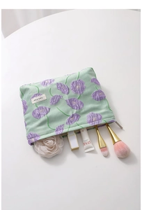 Detailed flat lay of floral canvas makeup bag with lipstick and brushes on a white table