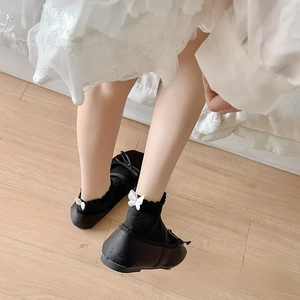 Detail of black Mary Jane shoes with matching socks featuring white bow accents