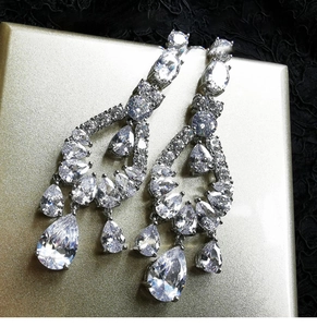 Macro shot of silver drop earrings with zircons on gold stand and black lace background