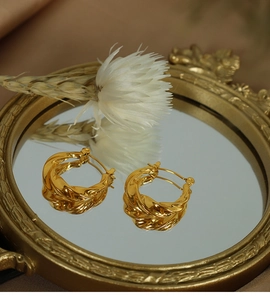 Détail des boucles d'oreilles créoles torsadées plaquées or 18k sur un plateau miroir
