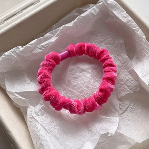 Detail view of a rose red velvet scrunchie showing soft chenille texture in a gift box