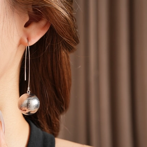 Détail d'une longue boucle d'oreille argentée avec sphère métallique texturée sur mannequin
