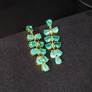 Dettaglio di lunghi orecchini a goccia verde smeraldo con montatura in oro e nappe