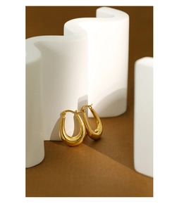 Detailed view of chunky golden oval earrings on a brown surface with geometric background