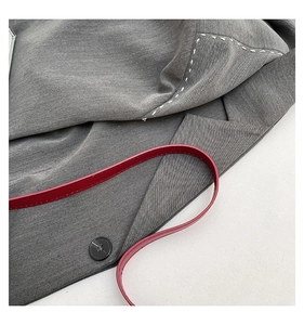 Detail shot of grey blazer lapel with white stitching, black button, and a red strap