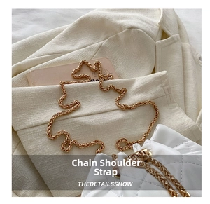Detail of white quilted bucket bag featuring a gold metal chain strap and drawstring closure