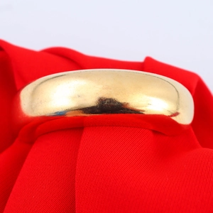 Elegante bracciale tondo in metallo lucido dorato su sfondo di seta rossa da donna