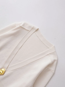 Detail of cream V-neck knit cardigan showing fine ribbed texture and gold irregular button