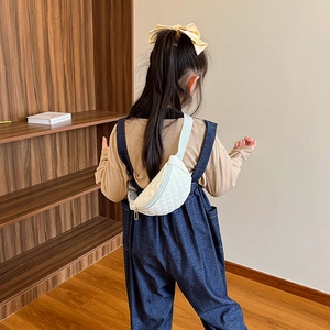 Kids white quilted chest bag with adjustable strap worn over denim overalls